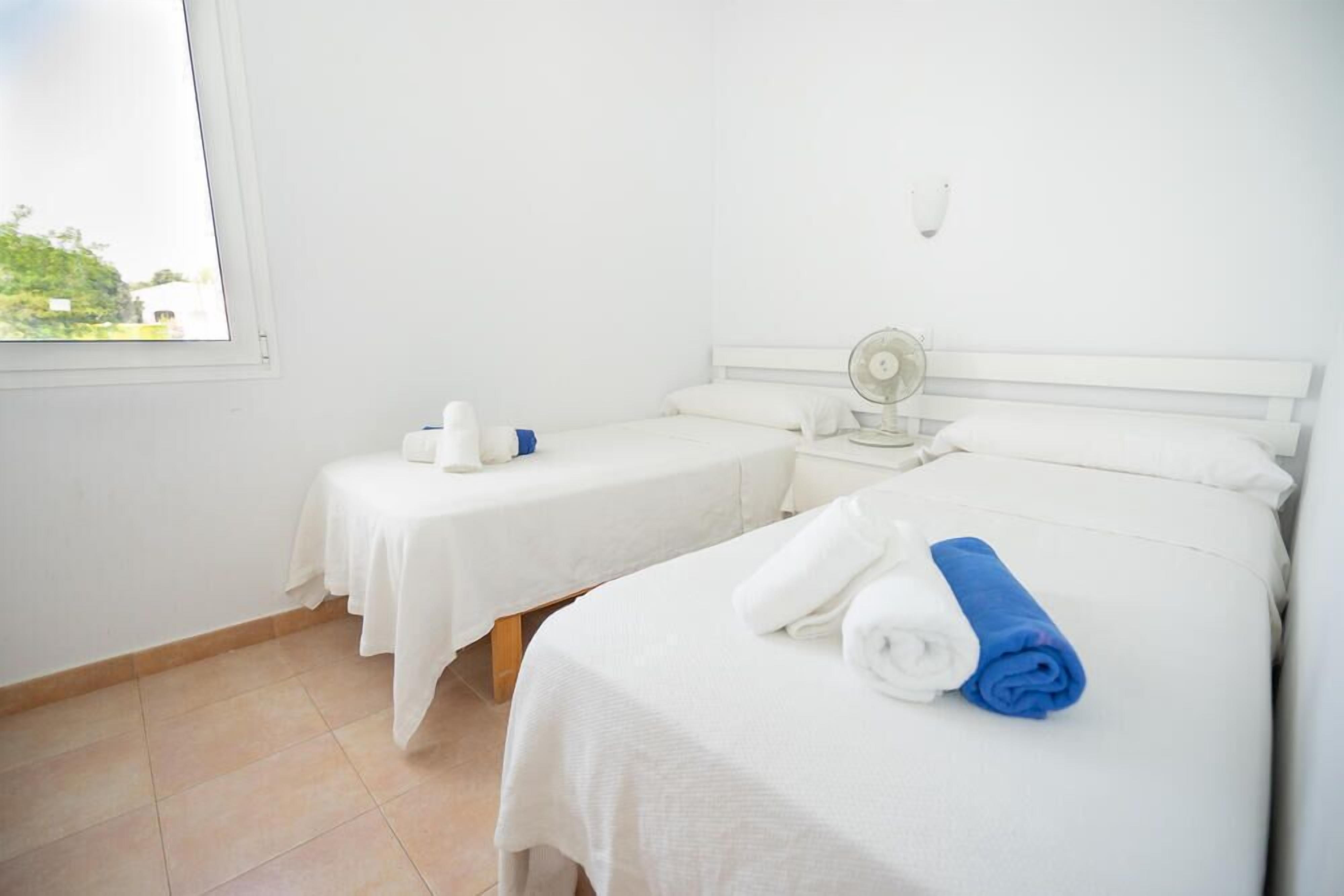 Une chambre d’hôtel avec deux lits, une fenêtre, une table de chevet avec un ventilateur et une vue sur la verdure.