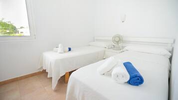 Habitación de hotel con dos camas, una ventana, una mesita de noche con un ventilador y vistas al exterior.