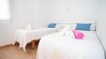 A hotel room with two single beds, each with a white bedspread and blue pillows. There are towels on the beds and a small table with a white tablecloth.