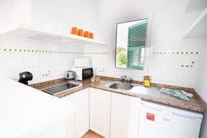 Una cocina moderna con gabinetes blancos, encimeras de granito, microondas integrado, tostadora y lavavajillas.