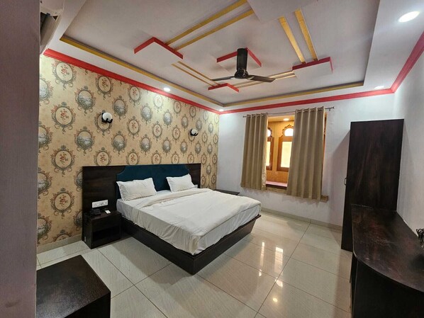 A bedroom with a bed, nightstands, a ceiling fan, and a window with curtains. - Hotel Sonal Niwas (Jaisalmer)
