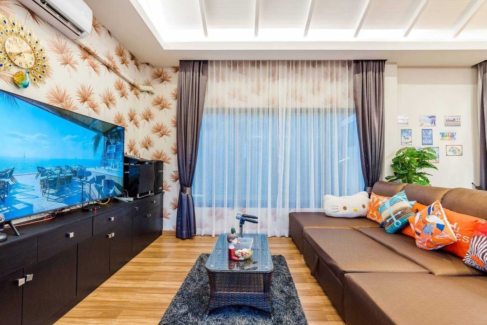 Una sala de estar moderna con un televisor de pantalla plana grande, un sofá, una mesa de centro y vista al mar a través de cortinas traslúcidas.