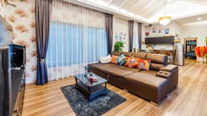 Ein modernes Wohnzimmer mit einer Sofagarnitur, einem Couchtisch und einem Fernseher. Im Hintergrund ist eine Küchenzeile mit Kühlschrank und Mikrowelle erkennbar.