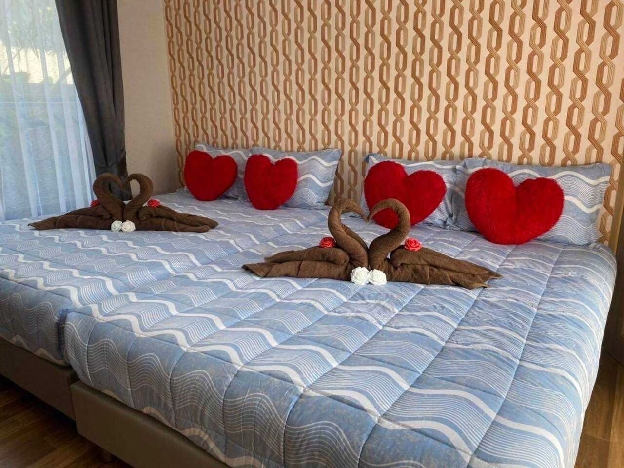 A bed with a patterned blue and white duvet, heart-shaped pillows, and a decorative arrangement of brown towels and flowers.