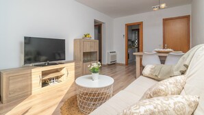 Een moderne woonkamer met een flatscreen televisie, een houten kast, een ronde witte tafel en een beige bank.