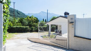 Una entrada con puerta, un paisaje de montañas al fondo, un pequeño edificio con un letrero con el número 905, y un cielo despejado.