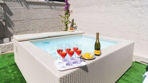 Un jacuzzi con una bandeja de bebidas rojas y una botella de champán.