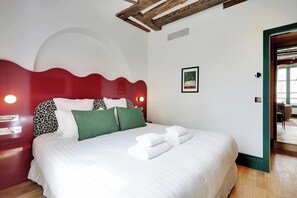 Un letto rifatto con lenzuola bianche e cuscini verdi, una testiera rossa e un quadro appeso alla parete.