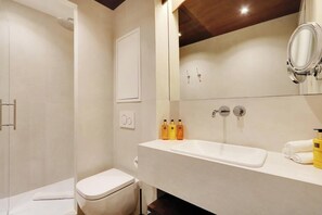 Un bagno moderno con doccia, WC e lavandino. Sul piano del lavandino sono presenti articoli da toilette.