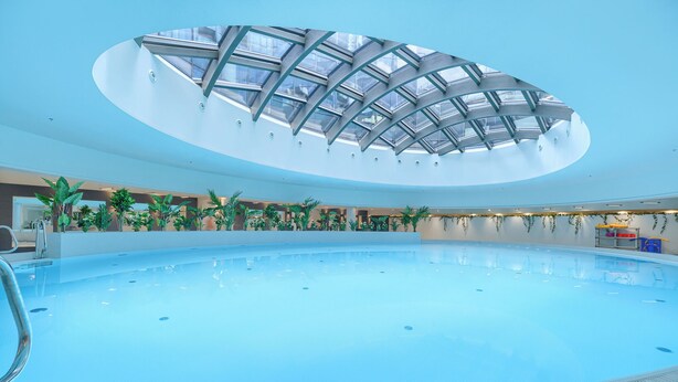 Une piscine intérieure dotée d’un toit en verre et entourée de verdure.