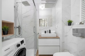 Un baño moderno con ducha de vidrio, lavamanos integrado y lavadora Samsung.