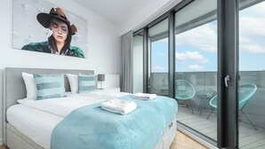 Une chambre moderne avec un grand lit, une vue sur le ciel par une porte-fenêtre coulissante et un balcon avec des chaises.