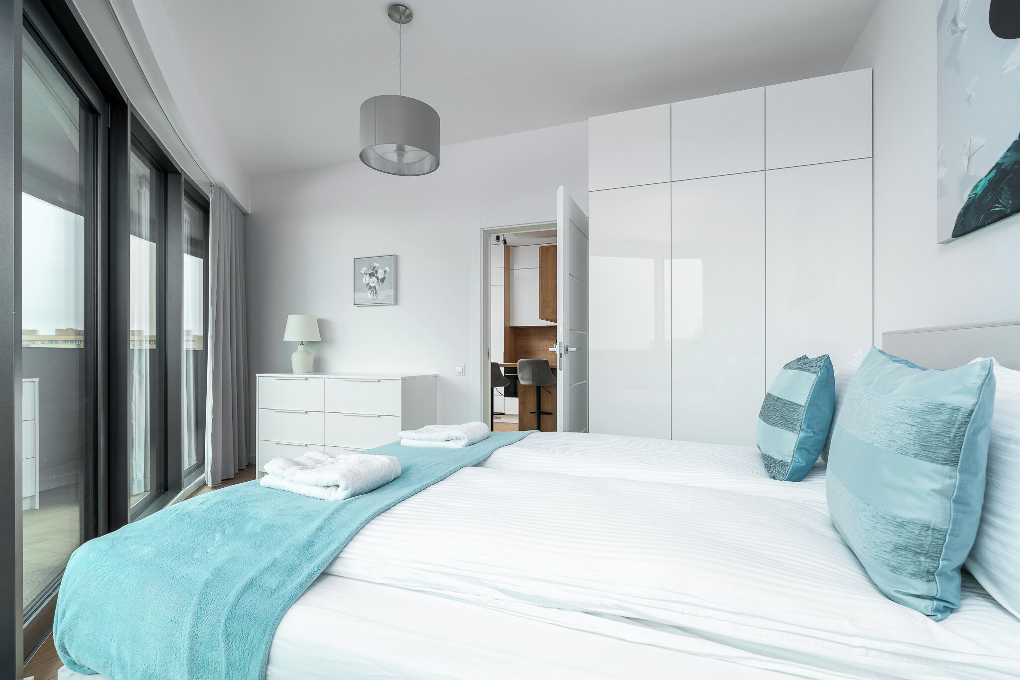 A modern bedroom with a large bed, a bedside table, a lamp, and a view of the outside.