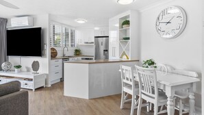 A modern kitchen with white cabinetry, a central island, and a dining area with white chairs and a table.