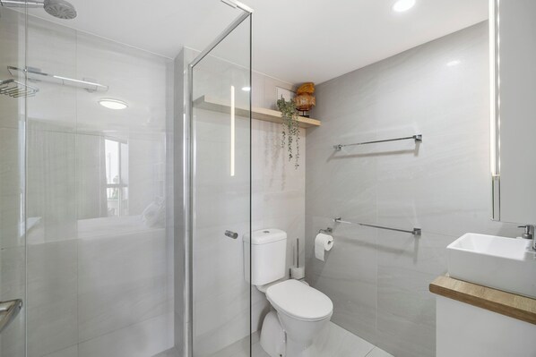 A modern bathroom with a glass shower enclosure, a toilet, a sink, and a mirror.