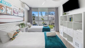 A modern hotel room with a bed, a massage table, a TV, and a balcony with plants.