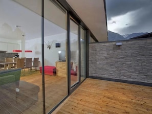 A modern interior with a wooden deck, a dining area with chairs and a table, and a kitchen with a red accent wall. - Stylish Neukirchen Home for 8 Guests (Neukirchen am Grossvenediger)