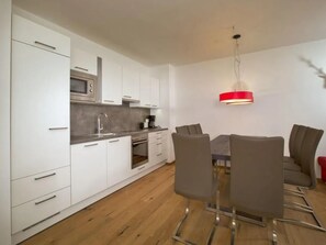A modern kitchen with white cabinets, a stainless steel microwave, and a red pendant light.
