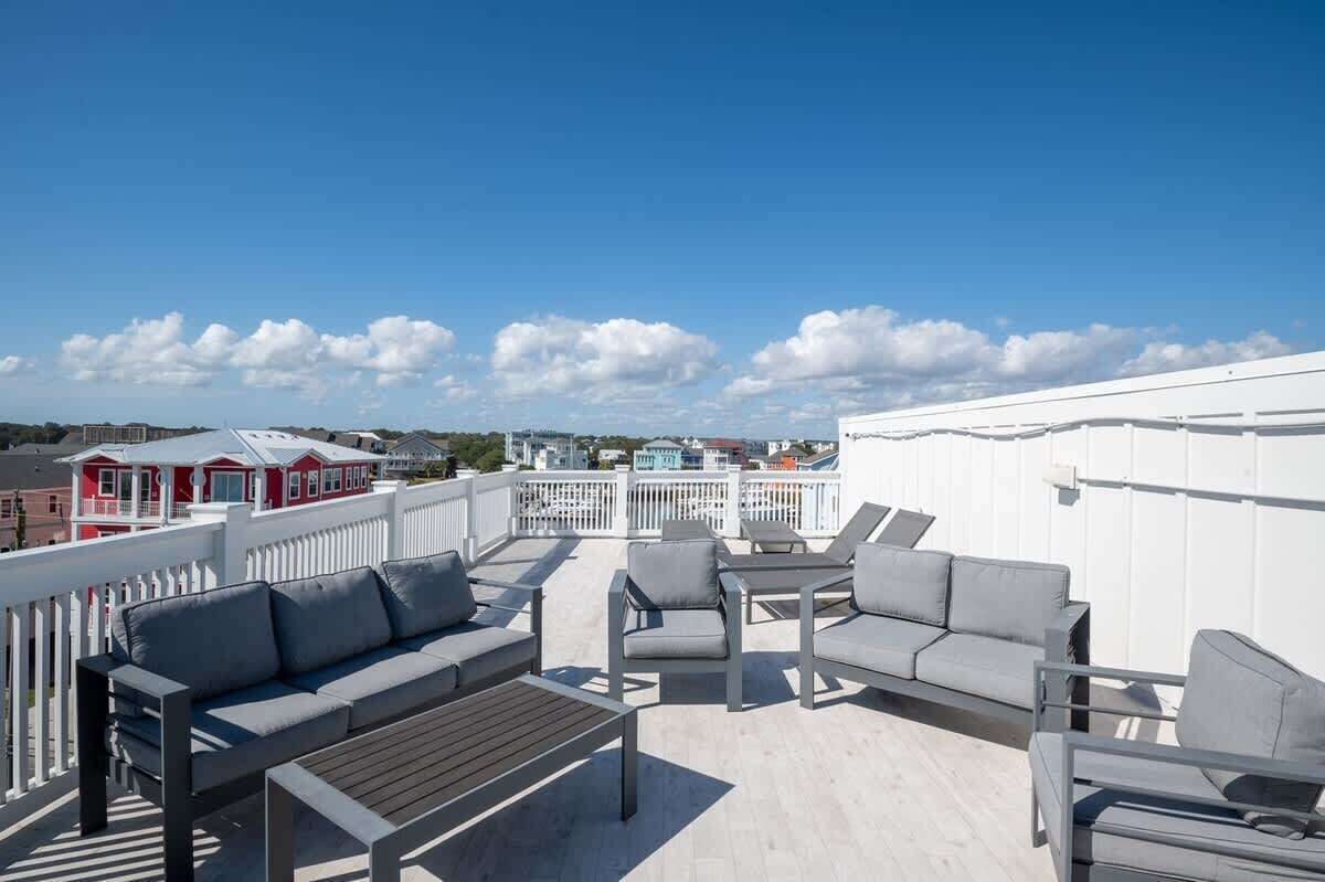 Une terrasse sur le toit, dotée d’un espace extérieur aménagé avec des sièges, une rambarde blanche et une vue sur les bâtiments en arrière-plan.