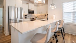 Una cocina moderna con armarios blancos, electrodomésticos de acero inoxidable y una isla central con taburetes de bar.