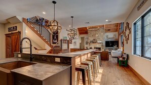 Una cocina moderna con una isla central, taburetes de bar, una escalera y una chimenea de piedra.