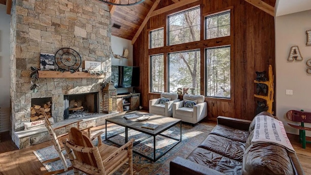 Una sala de estar acogedora con chimenea de piedra, ventanas amplias y vigas de madera rústica.