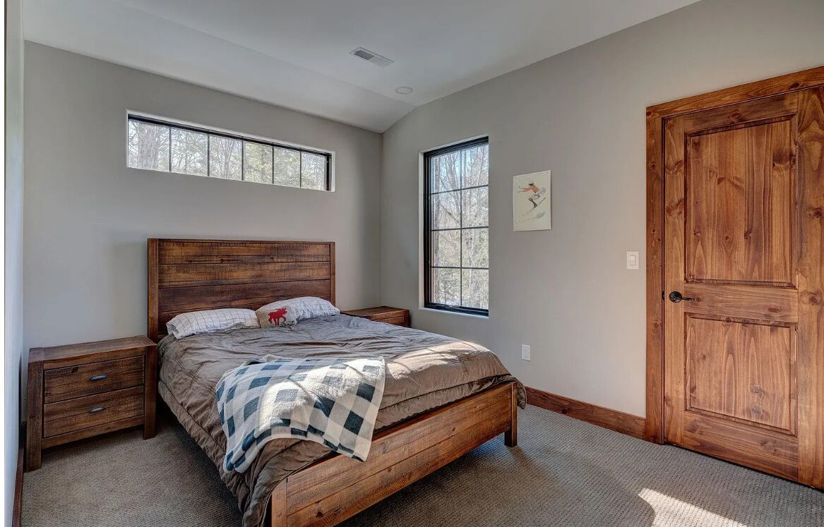 A bedroom with a wooden bed, two nightstands, a large wooden door, and two windows.
