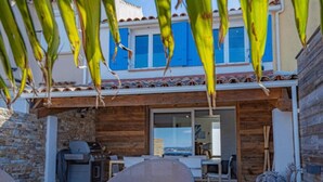 Fachada de madera con un muro de piedra, una terraza de madera y vista al mar.