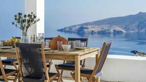 Une table en bois avec des chaises, un vase rempli de fleurs et une vue sur une côte montagneuse.
