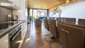 Cocina moderna con estufa, horno y hervidor, un comedor con sillas y un amplio ventanal con vistas al exterior.