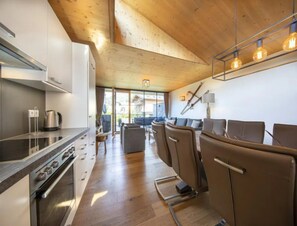 Een moderne keuken met een fornuis, oven en waterkoker, een eethoek met stoelen, en een groot raam met uitzicht op de omgeving.