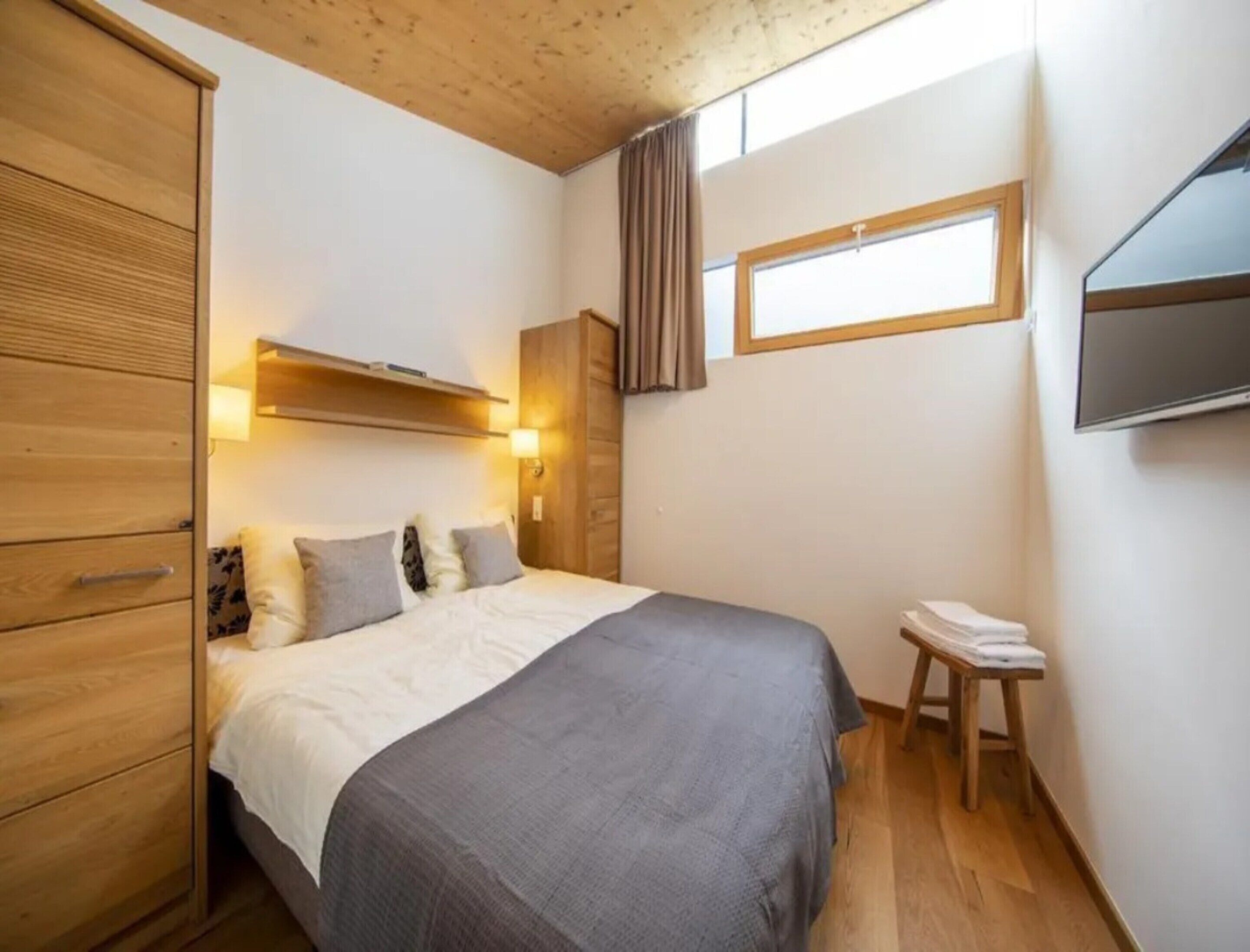 Une chambre à coucher comprenant un lit, une armoire en bois, une table de chevet et un téléviseur fixé au mur.