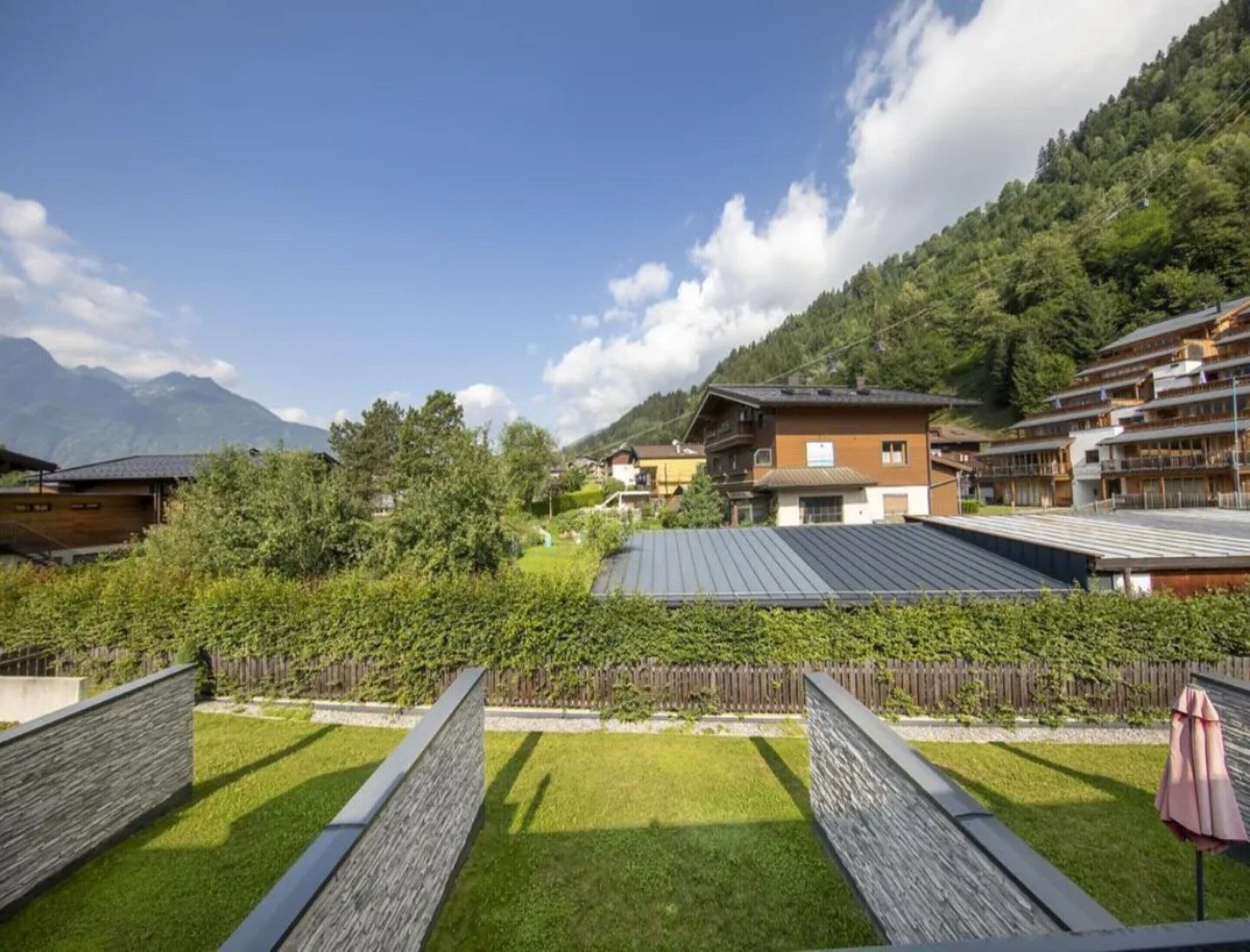 A hotel with a view of mountains, a wooden fence, and a grassy lawn.