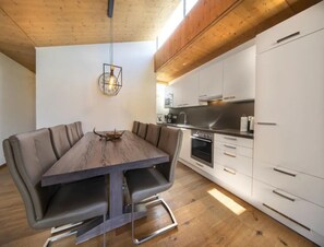 Une cuisine moderne avec des meubles blancs, des appareils en acier inoxydable et une table à manger en bois, accompagnée de chaises.