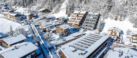 A snow-covered mountain town with modern buildings, a ski lift, and a dense forest in the background.