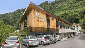 Un edificio moderno con fachada de madera y un letrero que dice 'residenz'. Hay varios coches estacionados adelante.