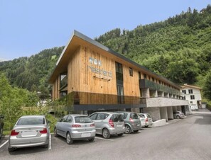 Een modern gebouw met een houten gevel en een bord waarop 'residenz' staat. Voor het gebouw zijn verschillende auto's geparkeerd.