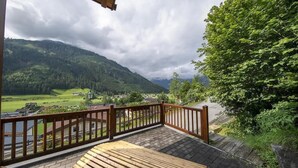 Une terrasse en bois, dotée d’une balustrade, qui offre une vue sur une vallée avec des maisons et de la végétation.