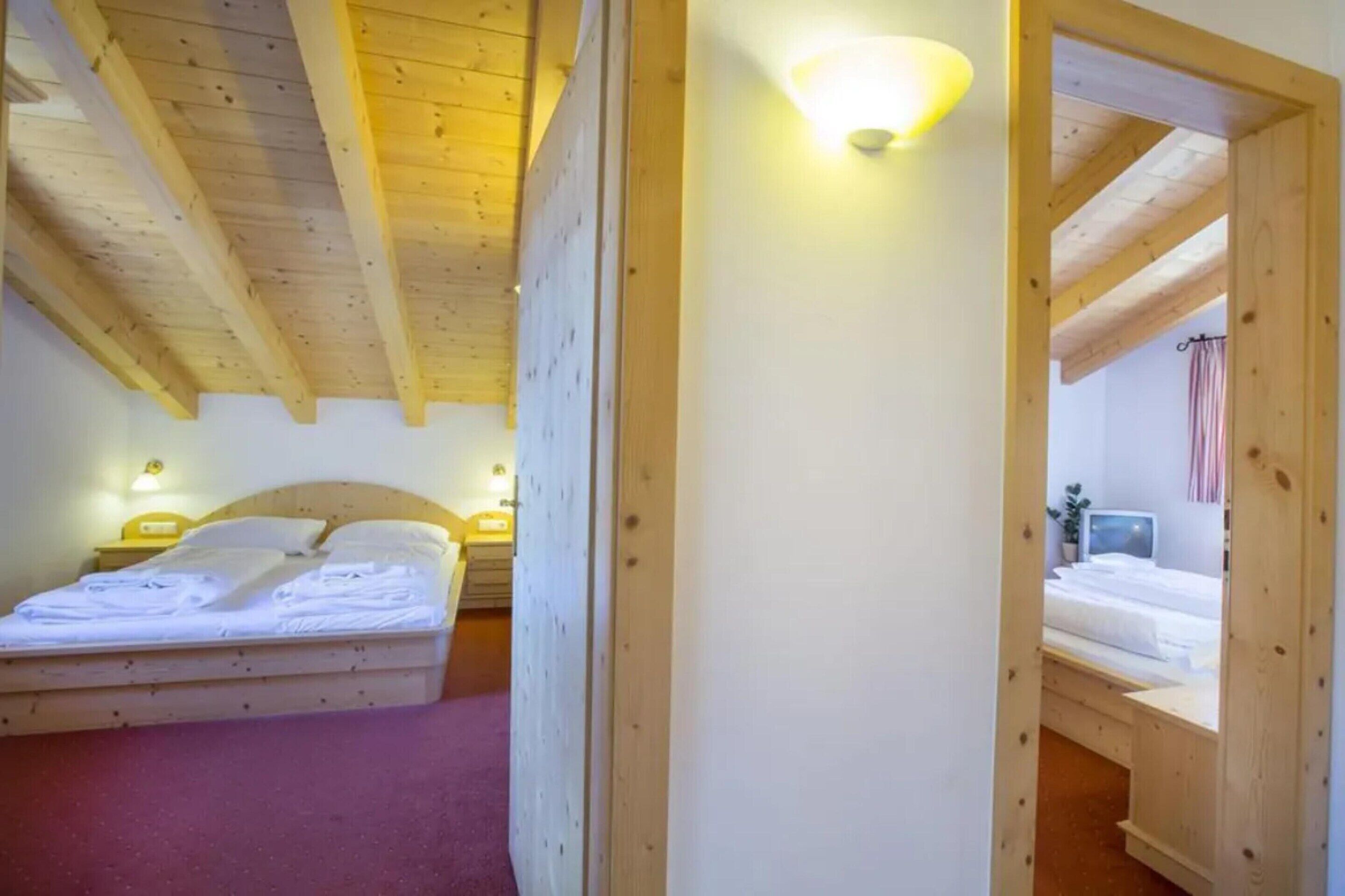 Ein Schlafzimmer mit Holzbalkendecke, einem Bett mit weißen Leinentüchern, einem Nachttisch mit Lampe und einem Fenster mit Vorhängen.