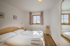 A bedroom with a wooden bed, a small chair, a window with curtains, and a mirror. - Panoramic Cottage in Wald im Pinzgau (Wald im Pinzgau)