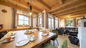 A wooden dining table with chairs, a chandelier, and a view of the outdoors through large windows.