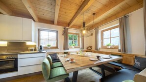 A cozy kitchen with a wooden ceiling, a dining table with chairs, and a view of greenery outside.