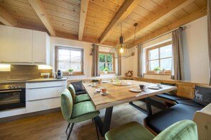 A cozy kitchen with a wooden ceiling, a dining table with chairs, and a view of greenery outside. - Panoramic Cottage in Wald im Pinzgau (Wald im Pinzgau)