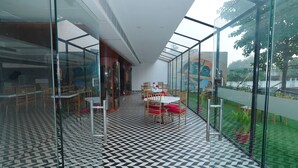 A modern indoor space with a checkered floor, glass walls, and a view of greenery outside. - Krishna Valley Wellness Resort Vrindavan (Mathura)