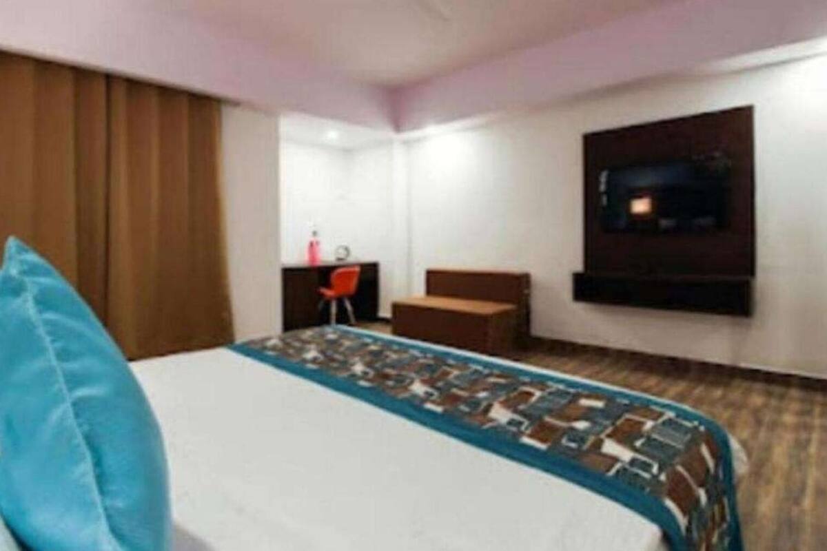 A hotel room with a bed, a desk, a chair, and a TV mounted on the wall.