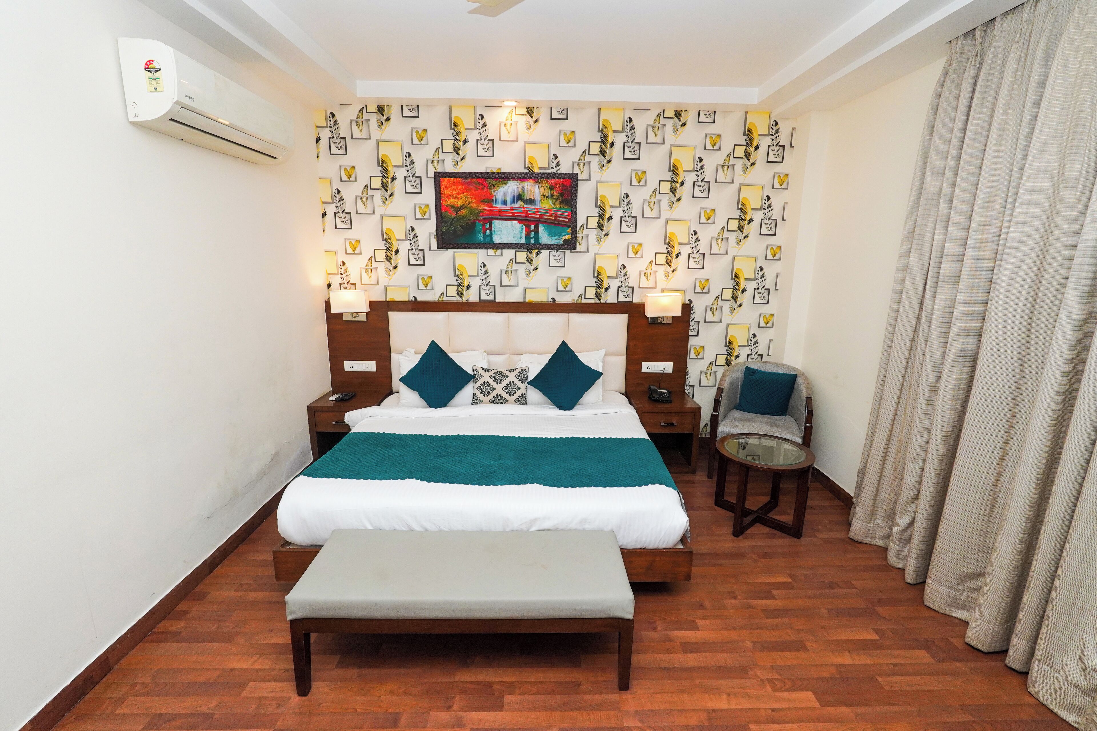 A hotel room with a bed, bedside tables, a bench, a chair, and a wall-mounted air conditioner.