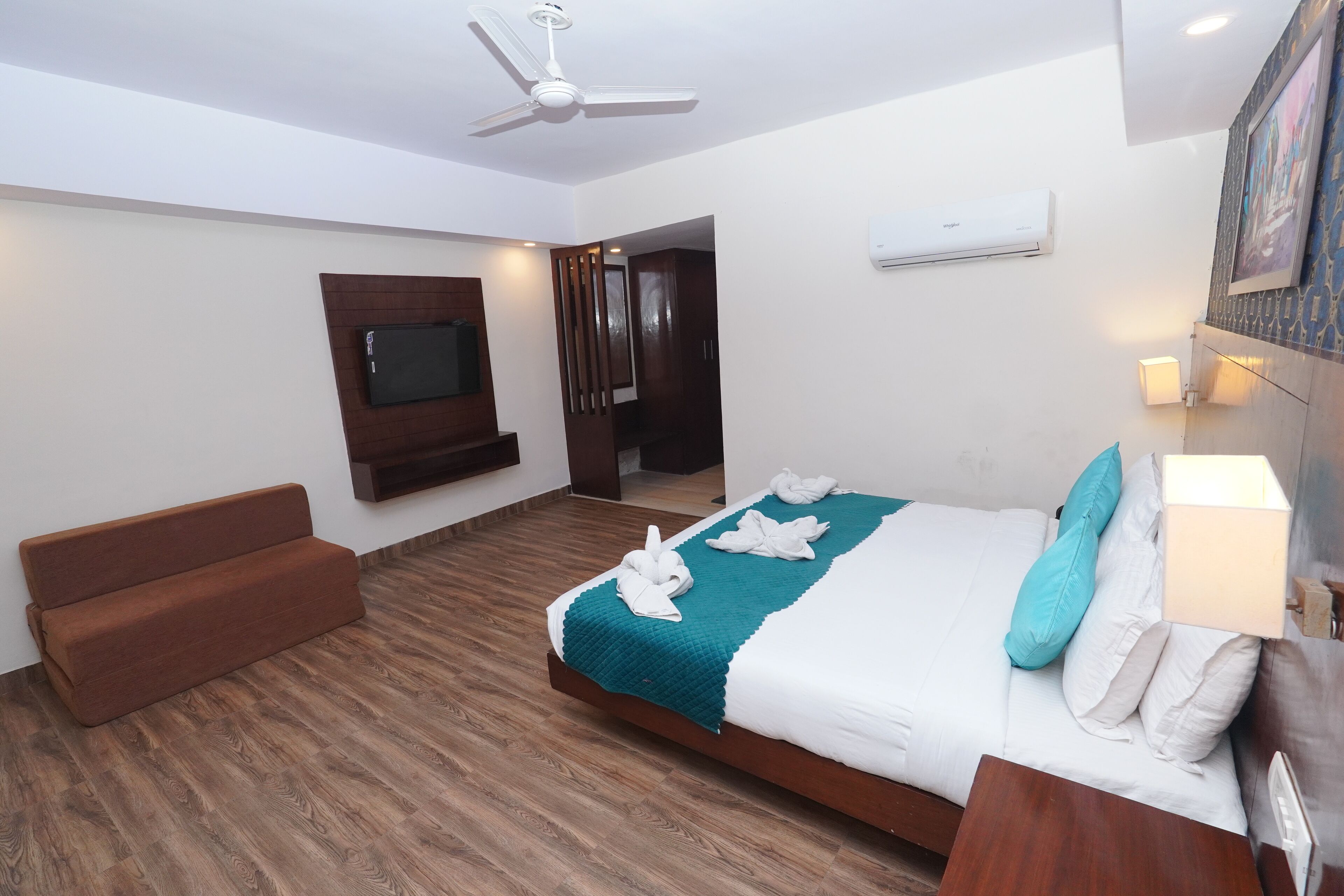 A hotel room with a bed, a sofa, a TV, and a ceiling fan.