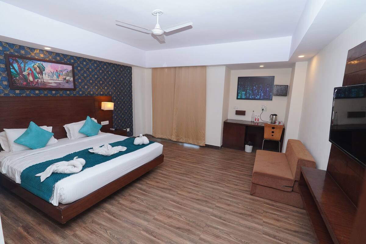 A hotel room with a large bed, a desk, a TV, and a ceiling fan.