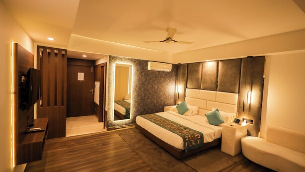 A modern hotel room with a large bed, a bedside table, a TV, and a ceiling fan. - Krishna Valley Wellness Resort Vrindavan (Mathura)