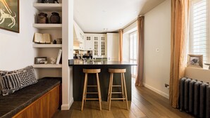 A modern kitchen with a central island, wooden stools, and built-in cabinets. - Welcome to your stylish retreat in the heart of Primrose Hill (London)